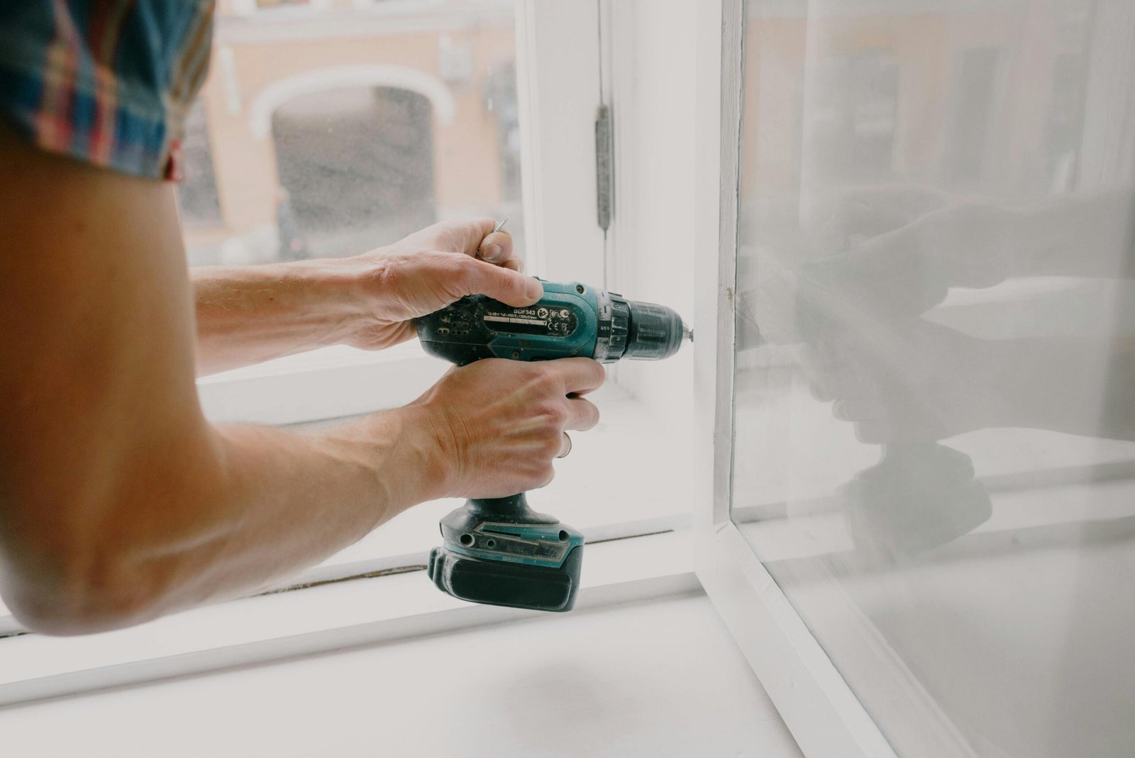 Nos Services A person using an electric drill to repair or install a window indoors.